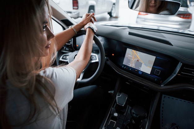 Esperando al gerente. Chica en coche moderno en el salón. Durante el día en interiores. Comprar vehículo nuevo