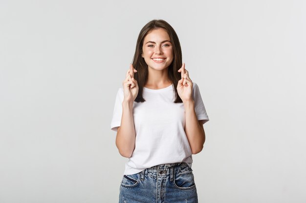 Esperanza sonriente niña cruza los dedos buena suerte, pidiendo deseos o rezando.