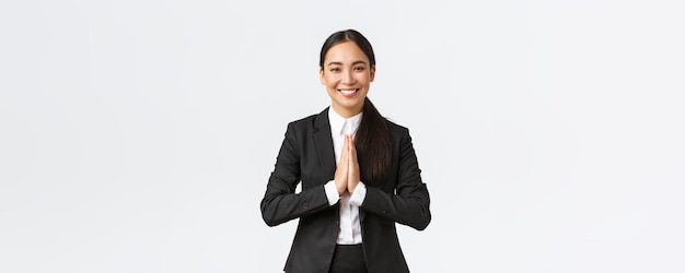 Foto gratuita esperanzada y alegre mujer de negocios asiática con traje negro inclinándose cortésmente y diciendo namaste saludando a los clientes y