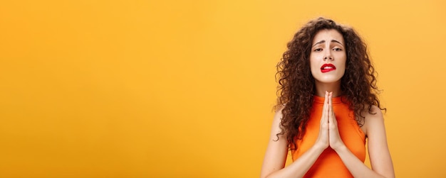 Foto gratuita esperanzadora mujer encantadora y tonta con corte de pelo rizado tomados de la mano en oración mordiéndose el labio inferior en necesidad