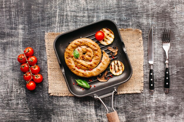 Espirales deliciosas salchichas a la parrilla en una sartén con vegetales sobre fondo de textura