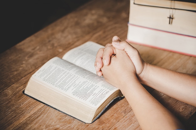 Espiritualidad y religión, las manos juntas en oración en una Santa Biblia en el concepto de iglesia para la fe.