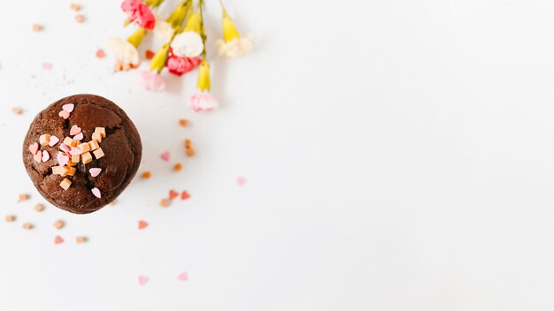 Espolvoree y caramelos caramelos en la magdalena del chocolate con la flor en el fondo blanco