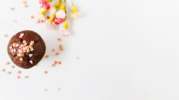 Espolvoree y caramelos caramelos en la magdalena del chocolate con la flor en el fondo blanco