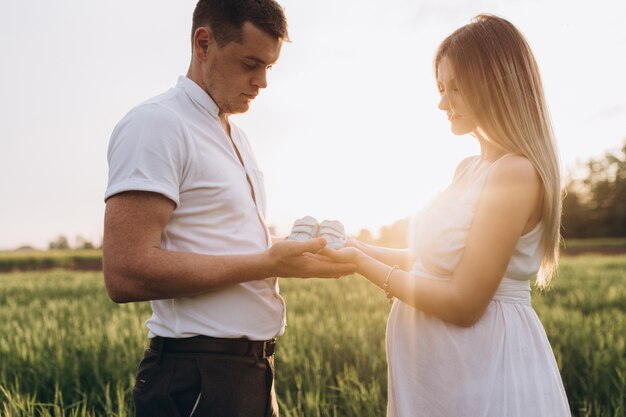 La esposa y el esposo manteniendo los zapatos de bebé y de pie en el campo