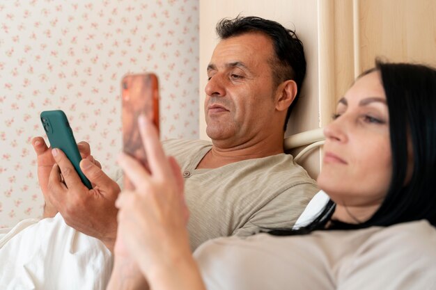 Esposa y esposo revisando su teléfono en la cama