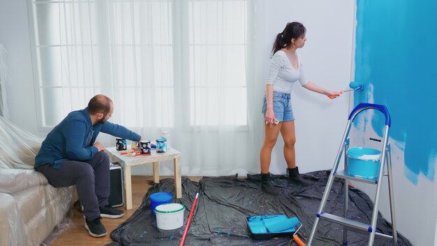 Esposa pintando la pared con un pincel durante la decoración del hogar. Pareja en decoración y renovación del hogar en acogedor apartamento, reparación y cambio de imagen