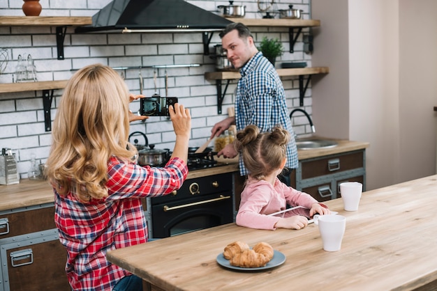 Foto gratuita esposa que toma la fotografía de su marido en el teléfono móvil mientras cocina en la cocina