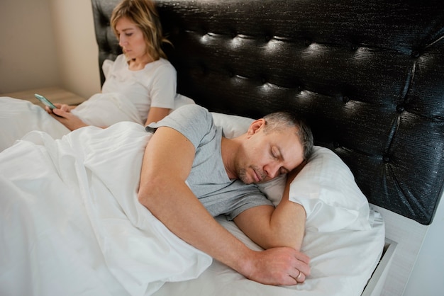 Foto gratuita esposa usando el móvil mientras su esposo está dormido