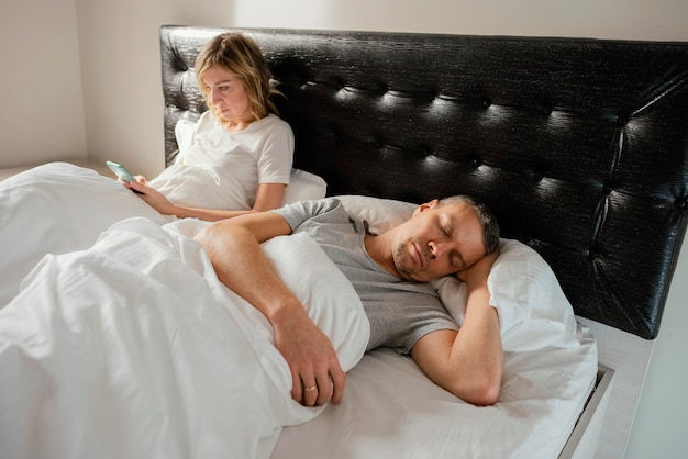 Esposa usando el móvil mientras su esposo está dormido