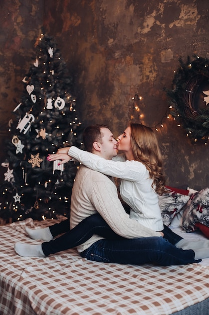 El esposo y la esposa caucásicos se relajan en una cama acogedora junto al gran árbol de Navidad