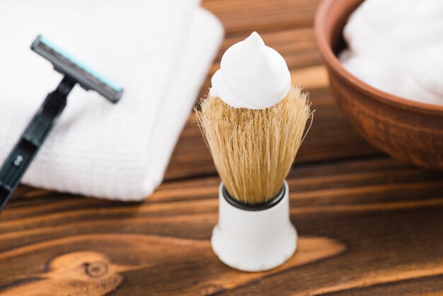Espuma blanca sobre la brocha de afeitar con maquinilla de afeitar; Servilleta y espuma sobre el escritorio.
