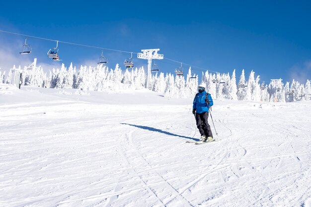Esquiador bajando la colina en el resort de montaña con teleféricos en el fondo