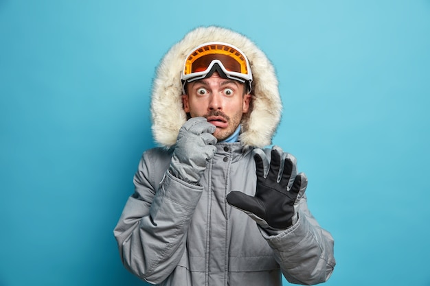 Foto gratuita esquiador masculino emocional asustado usa gafas de esquí de chaqueta cálida y guantes mira fijamente sorprendido tiene vacaciones de invierno activas pasa vacaciones en las montañas.