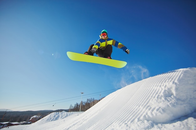 El esquiador de snowboarder saltando a través del cielo azul