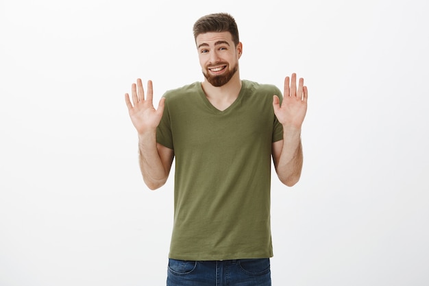 Está bien, cálmate, lo siento. Retrato de guapo joven barbudo que se siente incómodo disculpándose por la negativa levantando las manos en señal de rendición con una sonrisa tonta haciendo acusaciones y rechazando la oferta