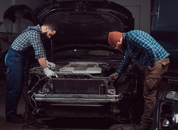 Estación de servicio. Dos mecánicos brutales barbudos reparando un coche en el garaje.