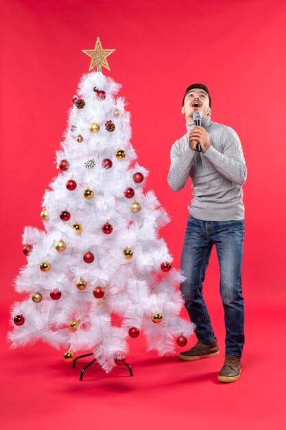 Estado de ánimo de año nuevo con chico positivo sorprendido vestido con jeans de pie cerca del árbol de Navidad decorado