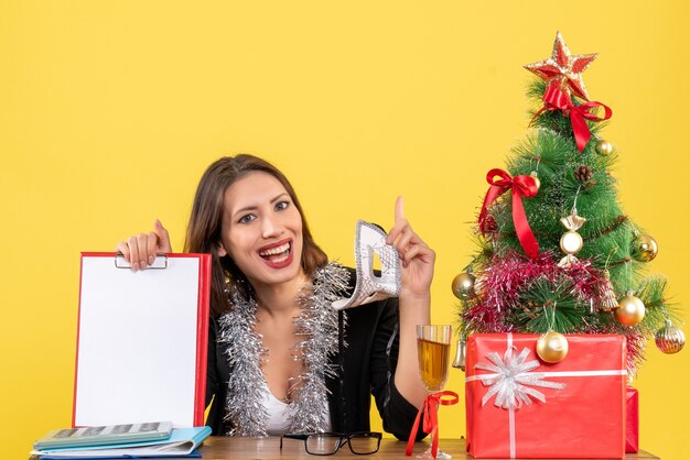 Estado de ánimo de año nuevo con una dama encantadora en traje sosteniendo una máscara y mostrando un documento apuntando hacia arriba en la oficina