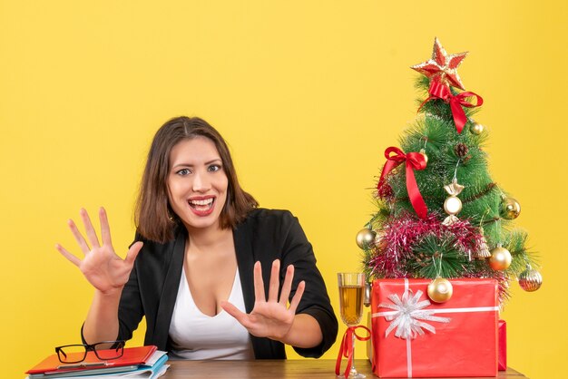 Estado de ánimo de año nuevo con hermosa dama de negocios mostrando diez y sentada en una mesa en la oficina