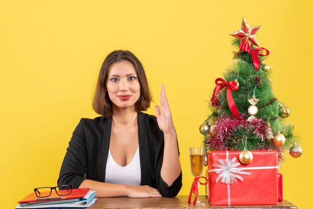 Estado de ánimo de año nuevo con una joven dama de negocios emocional feliz levantando la mano y sentada en una mesa en la oficina en amarillo