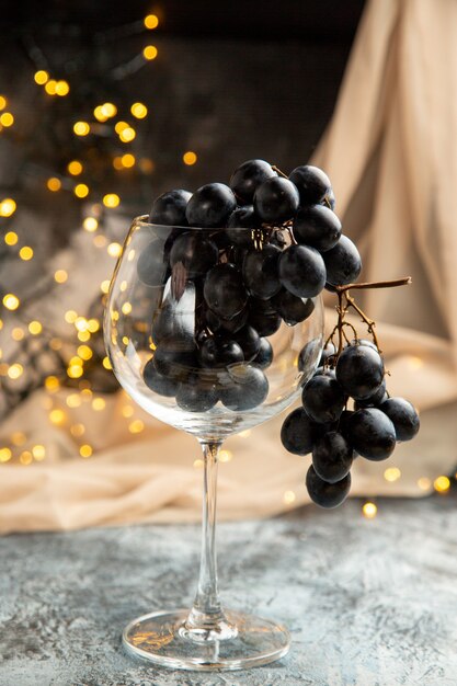 Estado de ánimo de año nuevo con uva negra en un vaso y una toalla de color nude sobre fondo oscuro