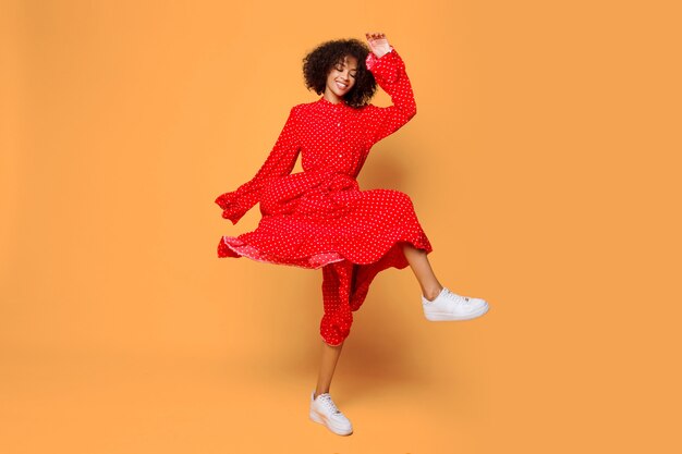 Estado de ánimo de ensueño. Chica africana con estilo bailando y saltando en naranja