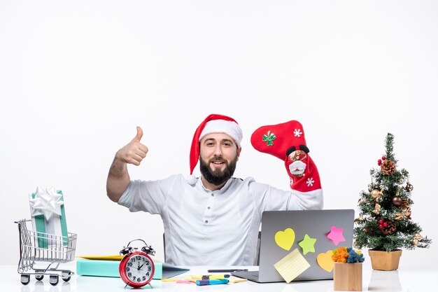 Estado de ánimo de Navidad con un adulto joven positivo con gorro de Papá Noel y usar un calcetín de Navidad en la mano en la oficina haciendo un gesto de ok