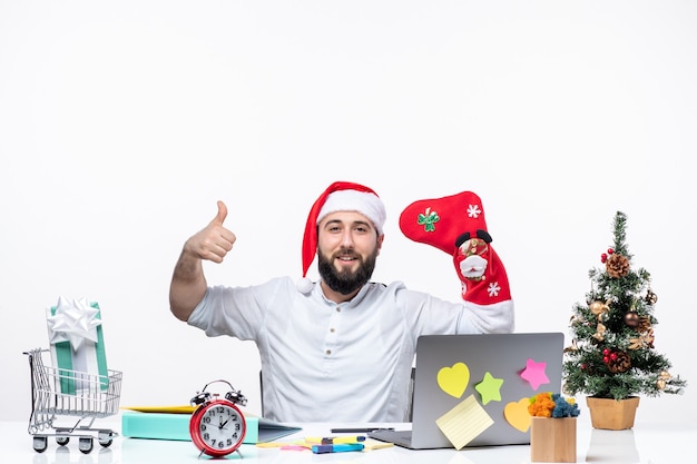 Estado de ánimo de Navidad con un adulto joven positivo con gorro de Papá Noel y usar un calcetín de Navidad en la mano en la oficina haciendo un gesto de ok