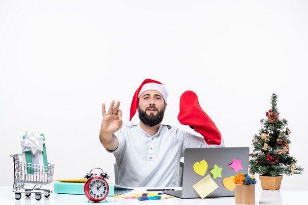 Estado de ánimo de Navidad con adultos jóvenes con gorro de Papá Noel y usar un calcetín de Navidad en la mano haciendo gesto de anteojos en la oficina