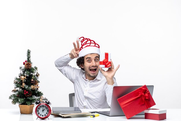 Estado de ánimo de Navidad con divertida persona de negocios con sombrero de santa claus levantando su regalo y mostrando dos sobre fondo blanco.