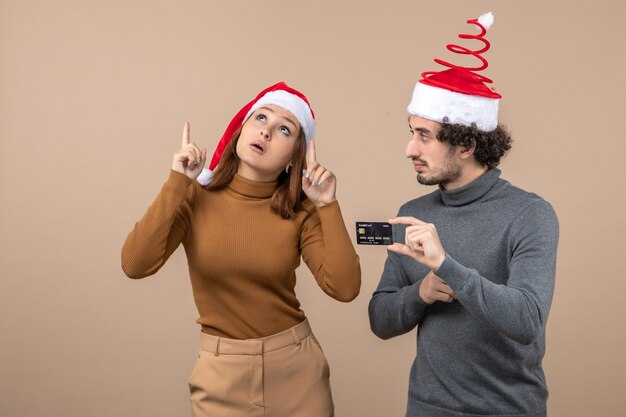 estado de ánimo de navidad con emocionado pareja fresca satisfecha con sombreros rojos de santa claus chico mostrando tarjeta bancaria