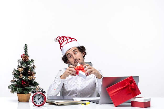 Estado de ánimo de Navidad con empresario sorprendido con sombrero de santa claus levantando su regalo y mirándolo sobre fondo blanco.