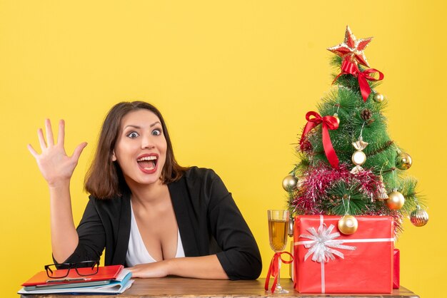 Estado de ánimo de Navidad con la joven dama de negocios emocional sonriente satisfecha mostrando cinco en amarillo