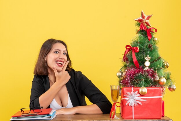 Estado de ánimo de Navidad con la joven dama de negocios feliz sentado en la oficina sobre fondo amarillo aislado