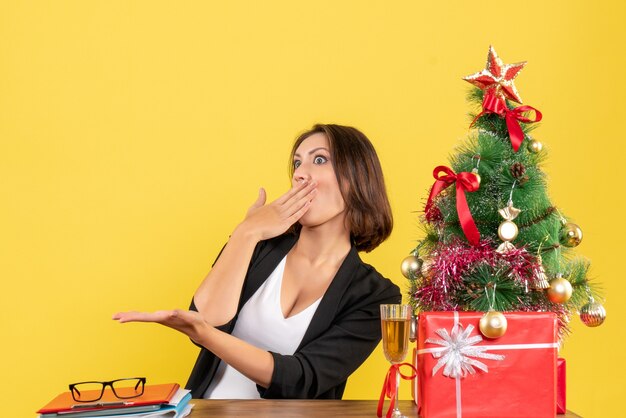 Estado de ánimo de Navidad con joven empresaria emocional sorprendida sentada en una mesa en la oficina en amarillo