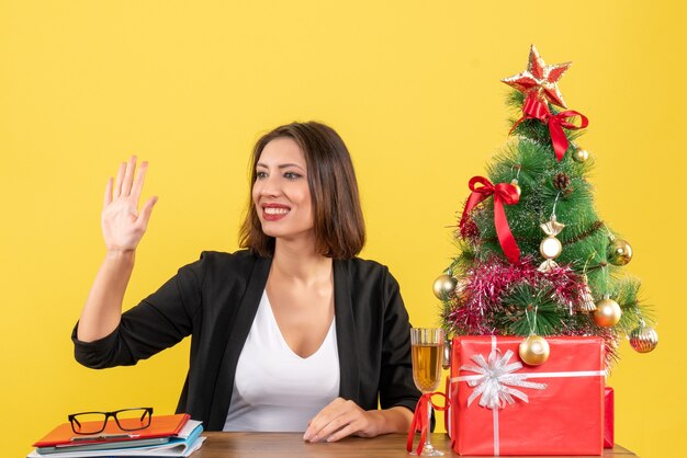 Estado de ánimo de Navidad con joven empresaria sonriente diciendo adiós felizmente en amarillo