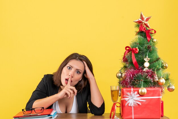 Estado de ánimo de Navidad con joven mujer de negocios serio cansado haciendo gesto de silencio en amarillo