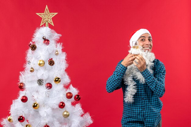 Estado de ánimo de Navidad con joven con sombrero de santa claus y levantando una copa de vino se alegra cerca del árbol de Navidad