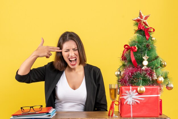 Estado de ánimo de Navidad con mujer de negocios emocional tensa enojada sentada en una mesa en la oficina en amarillo