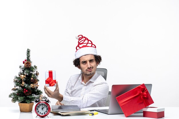 Estado de ánimo de Navidad con orgulloso joven empresario con sombrero de santa claus y sosteniendo su regalo de intercambio de ideas sobre fondo blanco.