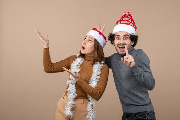 Estado de ánimo de Navidad con una pareja encantadora satisfecha fresca emocionada con sombreros rojos de santa claus apuntando arriba