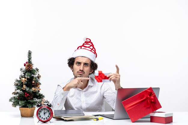 Estado de ánimo de Navidad con sorprendido empresario insatisfecho con sombrero de santa claus apuntando su regalo sobre fondo blanco.