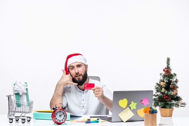 Estado de ánimo navideño con un adulto joven con sombrero de santa claus y sosteniendo una tarjeta bancaria y haciendo un gesto de llamarme en la oficina