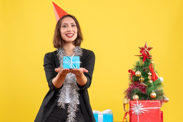 Estado de ánimo navideño con hermosa dama positiva con regalo felizmente en la oficina en amarillo