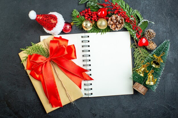 Estado de ánimo navideño con ramas de abeto, sombrero de santa claus, árbol de navidad, cinta roja en el cuaderno sobre fondo oscuro