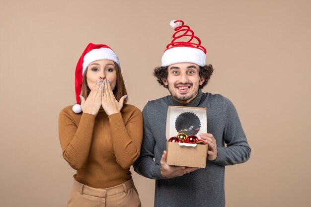 Estado de ánimo de vacaciones con pareja fresca emocionada con sombreros rojos de santa claus niña enviando beso en gris