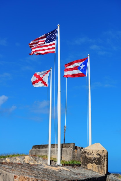 Foto gratuita el estado de puerto rico, el nacional estadounidense y la bandera de la ciudad de san juan vuelan con el cielo azul en el castillo de san juan el morro.