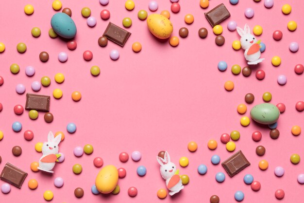 Estatuilla de conejito; caramelos de gema; Huevos de Pascua de chocolate con espacio en el centro sobre fondo rosa