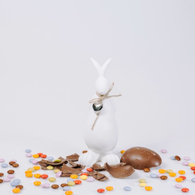 Estatuilla de conejito cerca de huevo de chocolate y pellets